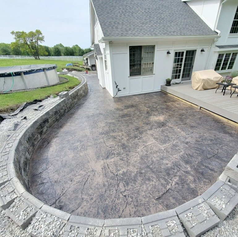An image of a stone wall and hardscaping around a stamped concrete patio.
