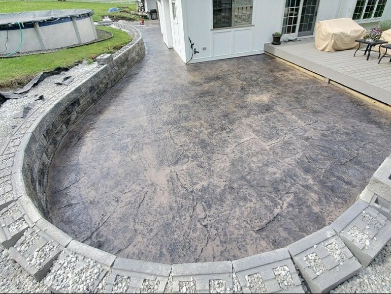 An image of a stone wall and hardscaping around a stamped concrete patio.